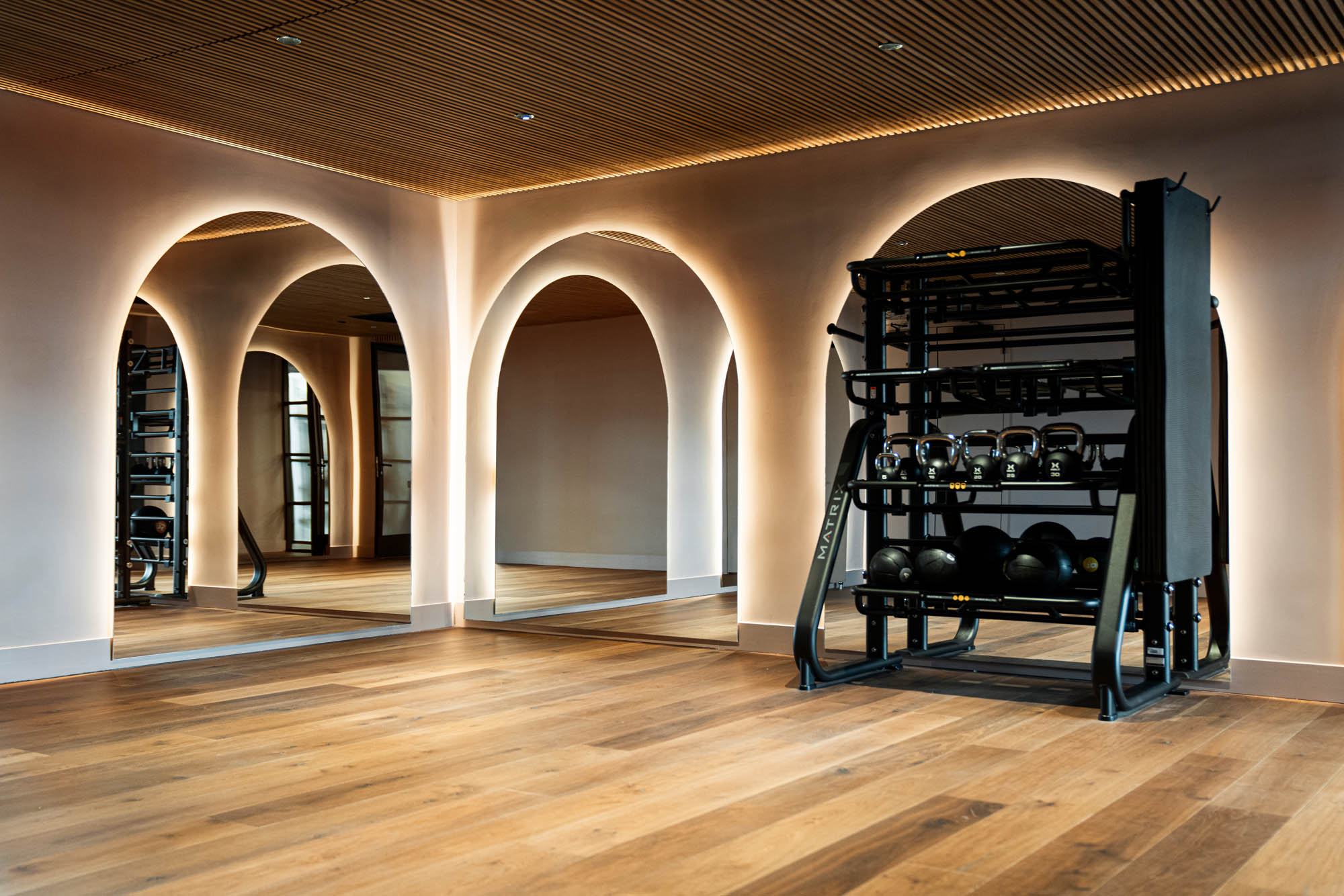 A fitness center with arch shaped back lit mirrors, a full dumbell stand, and wooden panel ceiling