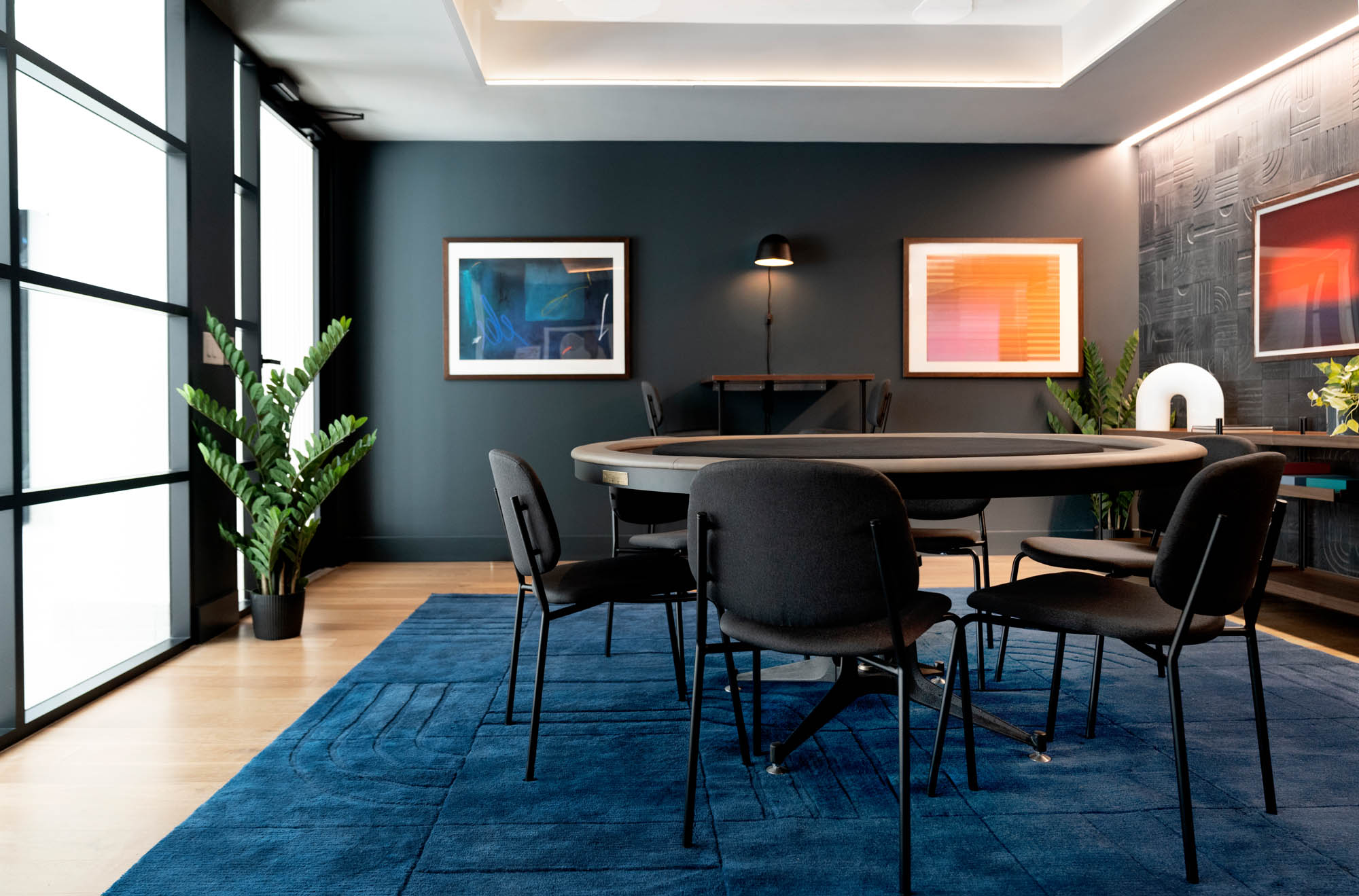 An cozy entertainment room with dark walls, a navy carpet, black chairs and a round gambling table in the middle