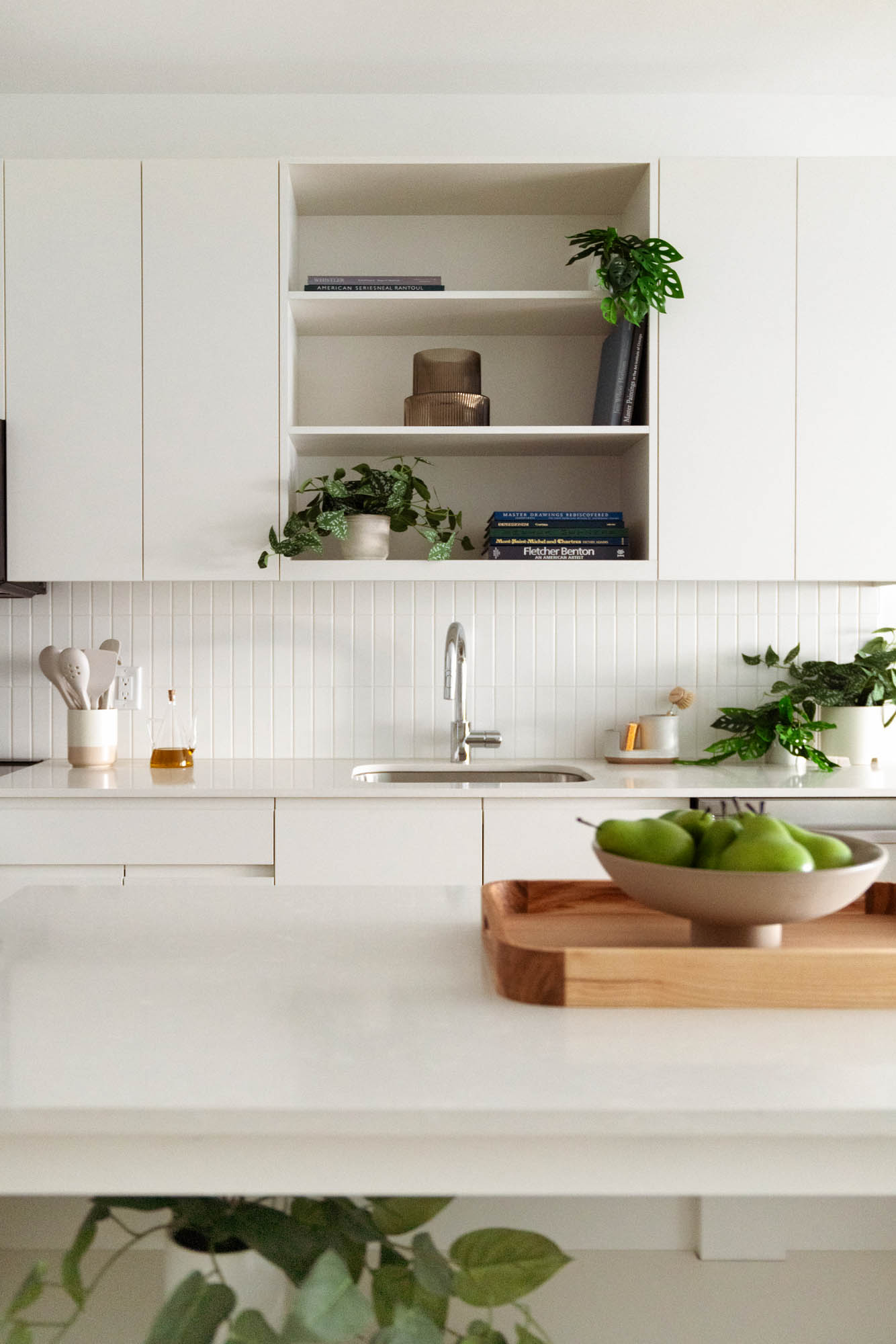 An off white kitchen with with cabinet and shelf space, an island, a sink and green decor